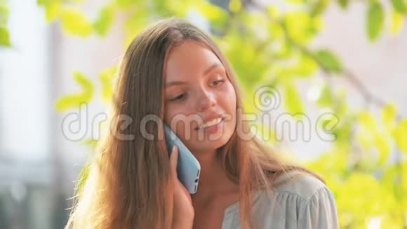 漂亮的年轻漂亮的女孩穿着蓝色衬衫带着蓝色的电话在夏天的稳定射击中说出来视频的预览图