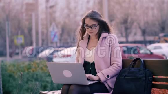 商务女性坐在长凳上在城市公园背景下使用笔记本电脑视频的预览图