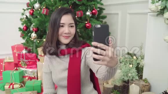 快乐的年轻亚洲女人使用智能手机自拍与圣诞树装饰她的客厅在家里圣诞节视频的预览图