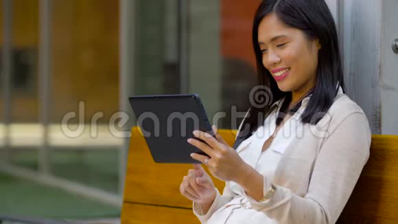 有平板电脑的亚洲女人坐在长凳上视频的预览图