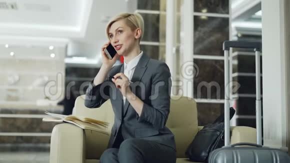 金发开朗的女商人坐在酒店大堂的扶手椅上手握笔一边说着手机视频的预览图