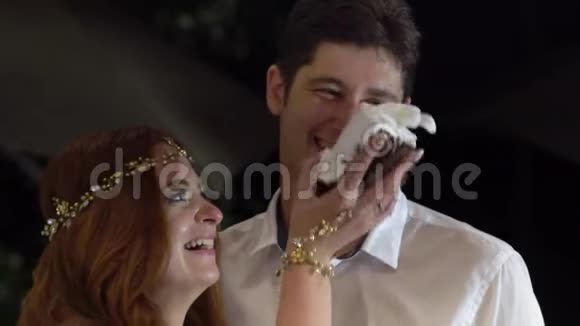 女孩在新郎的脸上涂抹一块结婚蛋糕婚礼的庆祝活动视频的预览图