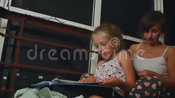 妈妈和女儿在睡觉前坐在夜窗附近女儿读了一本童话大书慢慢视频的预览图