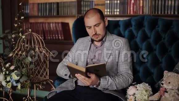 一个穿夹克的人坐在书柜背景的沙发上看书视频的预览图