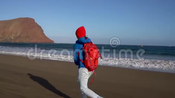 活跃的徒步旅行者女人在海滩上奔跑和跳跃西班牙加那利群岛特内里费带背包的高加索年轻妇女视频的预览图
