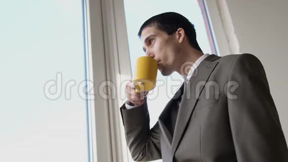 年轻英俊的商人喝着咖啡在办公室里站在窗边欣赏风景3840x21604k视频的预览图
