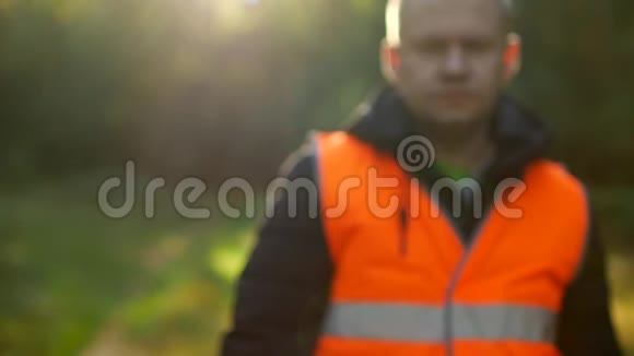 一个穿着橙色标志背心的人拿着一个包裹里面有自然森林特写和垃圾的背景视频的预览图