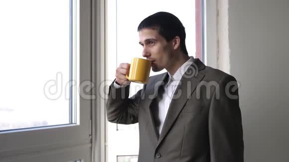 年轻英俊的商人喝着咖啡在办公室里站在窗边欣赏风景3840x2160视频的预览图