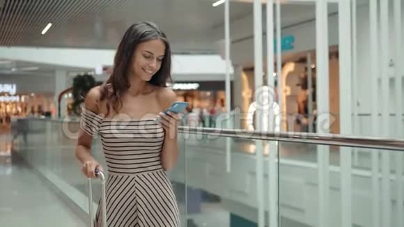 快乐的年轻女人在购物中心使用智能手机机场候机楼内有智能手机的女商务自由职业者视频的预览图