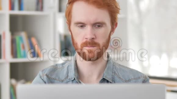 关闭在笔记本电脑上工作的临时红发男子视频的预览图