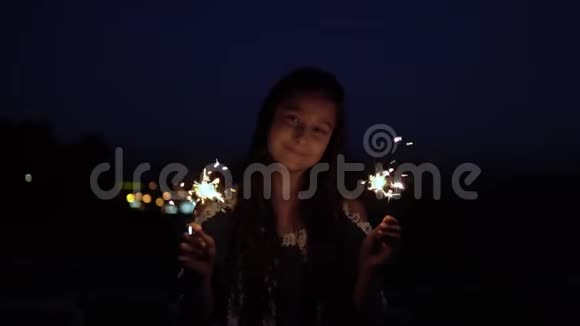 一个留着深色长发的年轻女孩在城市的背景下晚上拿着烟火高兴起来慢动作高清视频的预览图