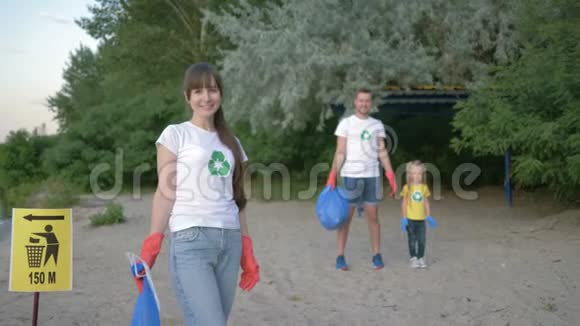 清洁海滩年轻志愿者母亲戴着橡胶手套的肖像背景上的指针标志附近有垃圾袋视频的预览图