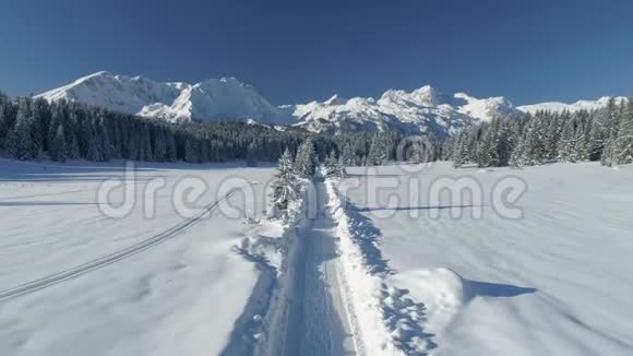 在阳光明媚的一天飞越一条雪域的乡间小路俯瞰群山视频的预览图