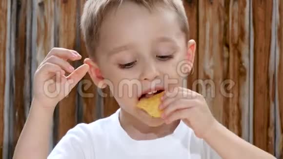 孩子坐在木墙背景的桌子旁高兴地吃着薯片视频的预览图