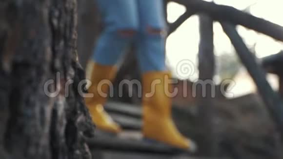 穿着黄色胶靴的人的腿走在森林里的木楼梯上穿着橡胶靴的脚视频的预览图