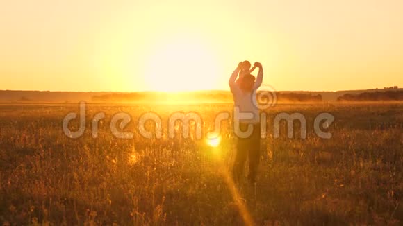 爸爸背着心爱的婴儿在日落时沿着田野走着视频的预览图