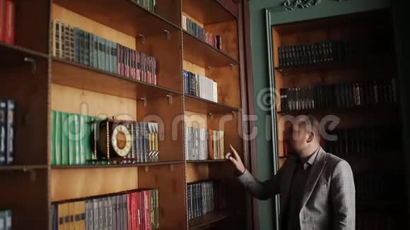 白人教授走在图书馆橱柜里看书架的肖像视频的预览图