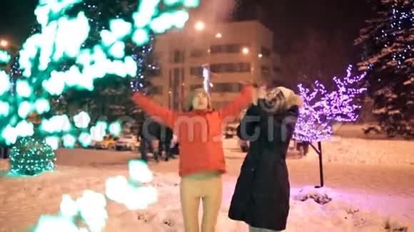 两个年轻的女孩在冬天穿过城市装饰的街道新年假日雪视频的预览图