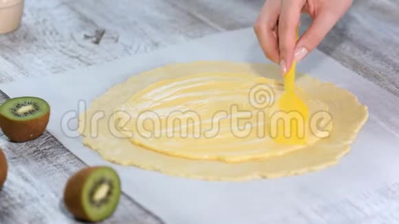 女性的手在生面团上涂上奶油用新鲜的猕猴桃做小面包视频的预览图