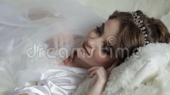 美丽可爱的新娘穿着睡衣躺在床上结婚的早晨漂亮整洁的女人微笑着慢动作视频的预览图
