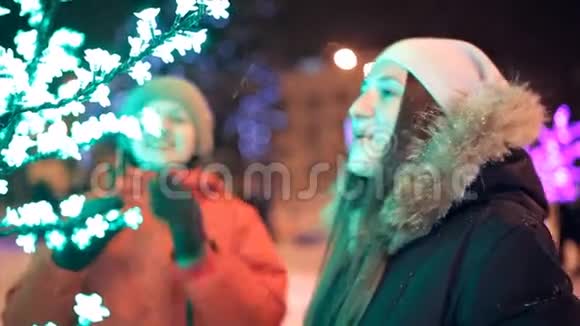 两个年轻的女孩在冬天穿过城市装饰的街道新年假日雪视频的预览图