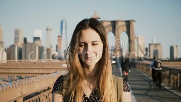 年轻的欧洲旅游女孩背包在相机摆姿势触摸头发和微笑布鲁克林大桥纽约4K视频的预览图