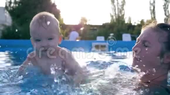 妈妈和孩子一起在游泳池里快乐的小男孩在夏天炎热的日子里做着飞溅的水视频的预览图
