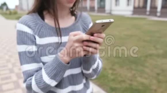 不可辨认的黑发女人正在手机上读一些东西走在家附近视频的预览图