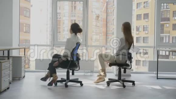 办公室工作人员两个年轻的女人坐在椅子上手里拿着文件高兴地看着对方笑着视频的预览图