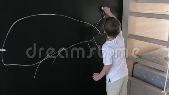 男孩在托儿所的石板墙上画画孩子用粉笔画黑墙视频的预览图