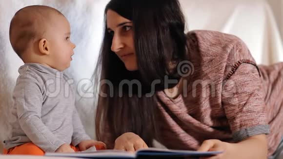 一位年轻快乐的母亲看着她的小儿子微笑着一位有爱心的母亲给她的孩子读童话故事视频的预览图