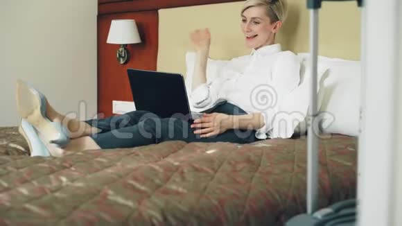 快乐女商人通过在线视频聊天与家人交谈使用笔记本电脑躺在酒店房间的床上旅费视频的预览图