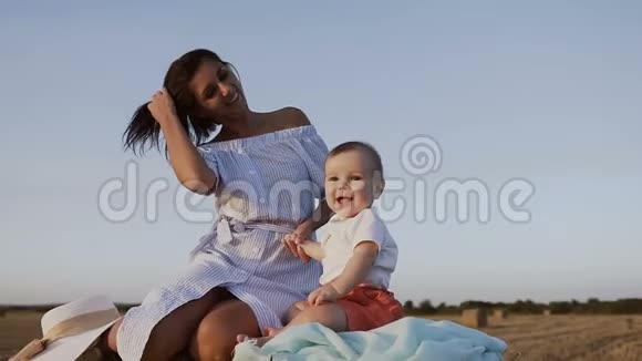 一个快乐的婴儿和他的母亲坐在田野里的稻草的肖像年轻女子带着儿子散步视频的预览图
