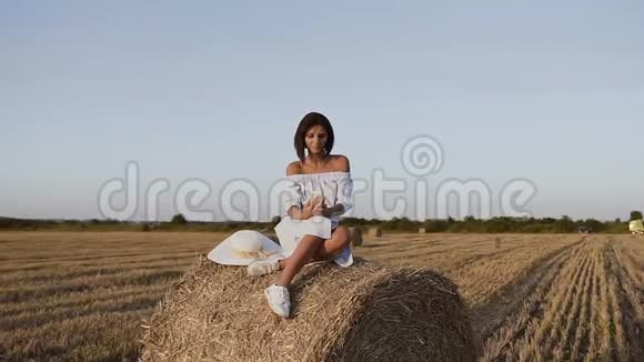 在意大利托斯卡纳的干草场上漂亮的年轻女子穿着蓝色连衣裙用电话享受大自然女孩玩得开心视频的预览图
