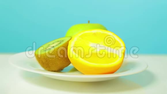 一个完整的绿色苹果和半个猕猴桃和橘子在一个白色的盘子里旋转成一个圆圈视频的预览图