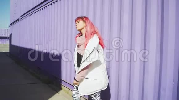快乐的年轻时髦女人粉红色的头发在彩色背景上跳舞美丽的女人在紫色的容器旁缓慢地跳舞视频的预览图