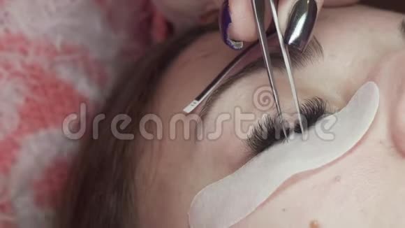睫毛延伸化妆师拿着钳子把人造睫毛贴在女人眼睛上极端的近距离视频的预览图