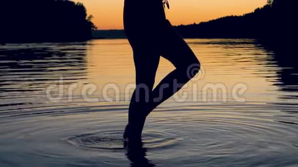 女人优雅地双脚抚摸日落湖中的水面膝盖视频的预览图