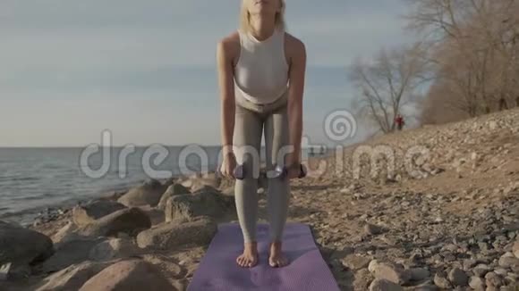 年轻的运动美女手里拿着哑铃在大海的背景上健身女孩做运动视频的预览图