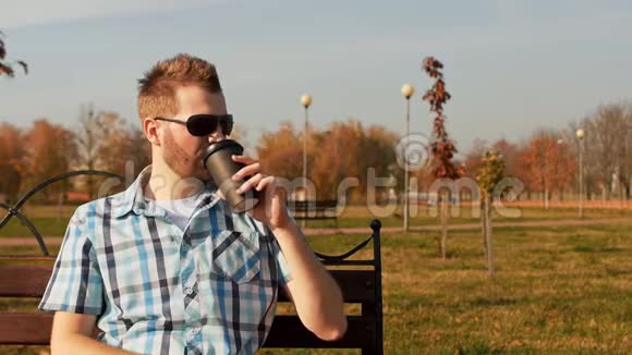 戴墨镜的时髦大胡子坐在长凳上喝咖啡视频的预览图