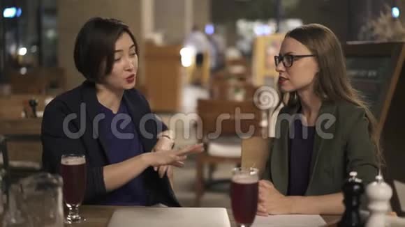 两个年轻的女朋友在户外咖啡馆里聊天视频的预览图