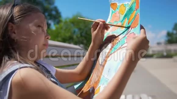 夏日儿童画家用画笔和水彩坐在长凳上画画视频的预览图