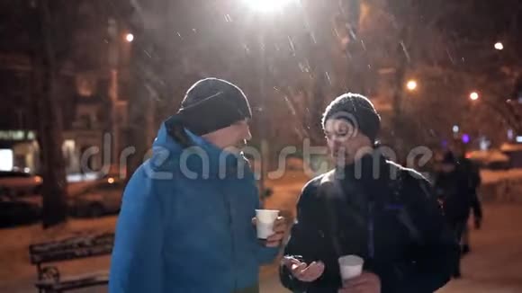 冬天两个年轻人站在街上大雪纷飞聊天喝咖啡视频的预览图