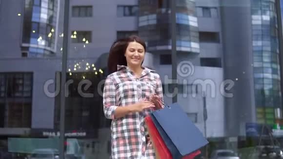年轻女孩购物后手里拿着包在购物中心附近心情很好慢动作视频的预览图
