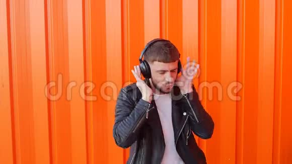 年轻的白种人戴着音乐耳机听着橙色背景的音乐和舞蹈Prance慢动作耳机视频的预览图