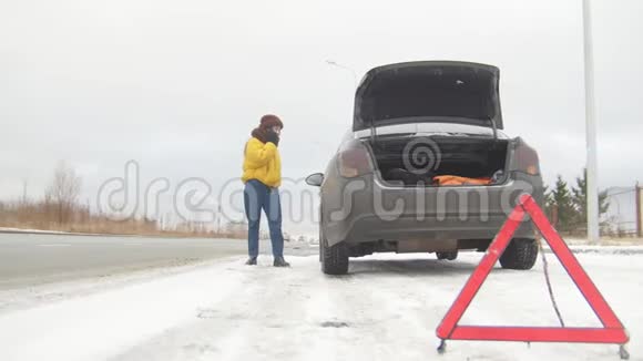 汽车故障紧急信号在下雪的乡间小路上遇到了汽车故障冬天一位年轻女子呼叫救援服务视频的预览图