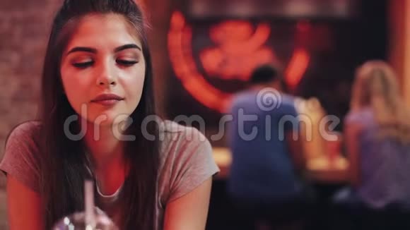 年轻女子坐在酒吧里喝着莱曼纳德看着镜头在交流中享受夜生活的女人视频的预览图