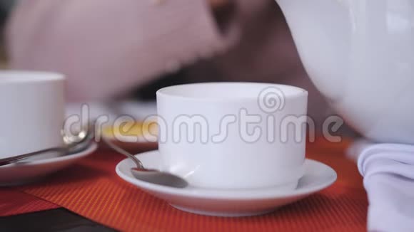 在餐厅的一张桌子上站着一个白色的杯子里倒着热绿茶的女人特写镜头视频的预览图