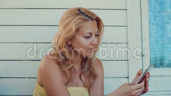 金发女人用手机打字在夏季露台休息视频的预览图