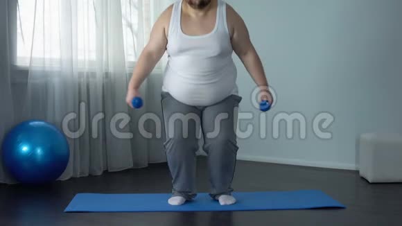 超重男子蹲在垫子上举起哑铃全身训练回家视频的预览图
